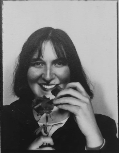 Black and white portrait of the artist with a rose in her hand. She is smilling.