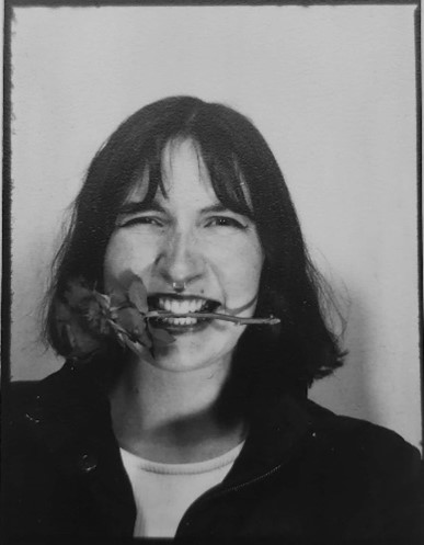 Black and white portrait of the artist. She is holding the rose between her teeth. 